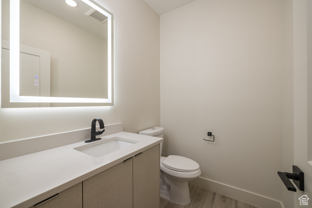Bathroom featuring toilet, vanity, wood finished floors, and baseboards