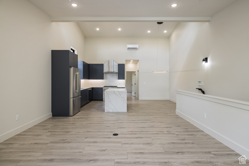 Kitchen with stainless steel appliances, wall chimney exhaust hood, light countertops, recessed lighting, and dark cabinetry