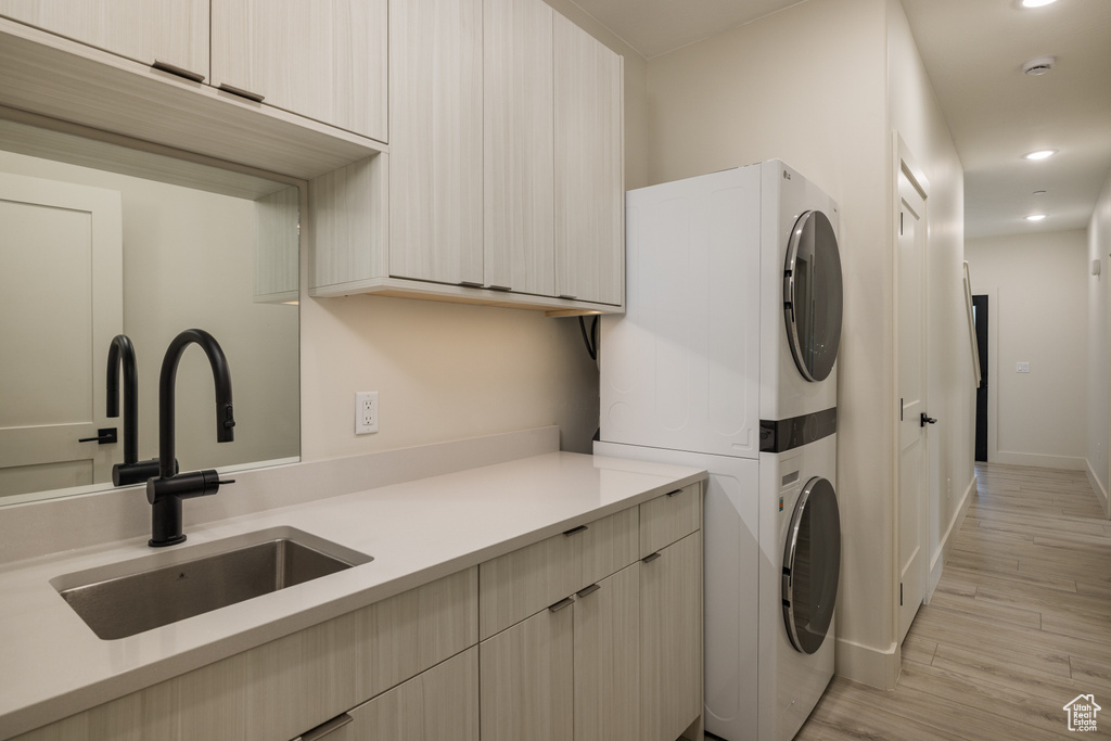 Washroom featuring stacked washer and clothes dryer, light wood-type flooring, recessed lighting, cabinet space, and baseboards
