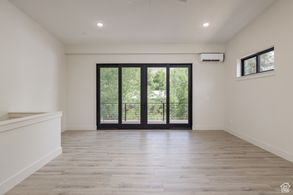 Empty room featuring a wall mounted AC, recessed lighting, light wood-style flooring, and baseboards