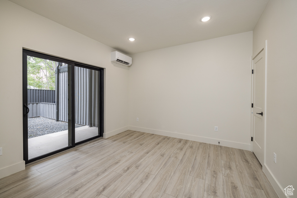 Empty room featuring a wall mounted AC, light wood-style floors, baseboards, and recessed lighting