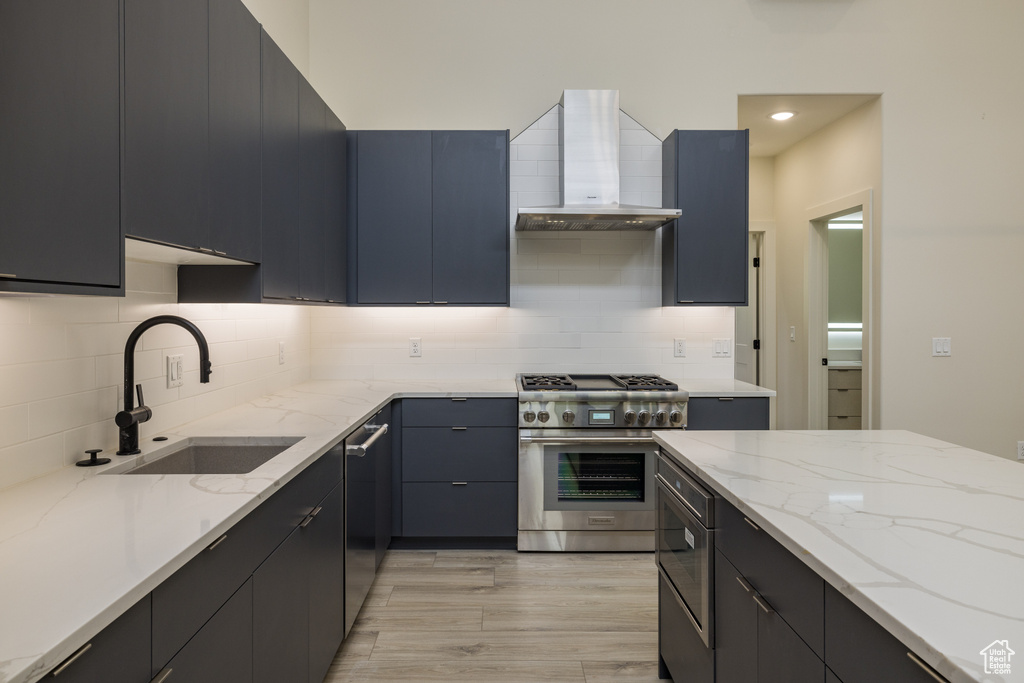 Kitchen featuring appliances with stainless steel finishes, wall chimney exhaust hood, a sink, backsplash, and dark cabinetry
