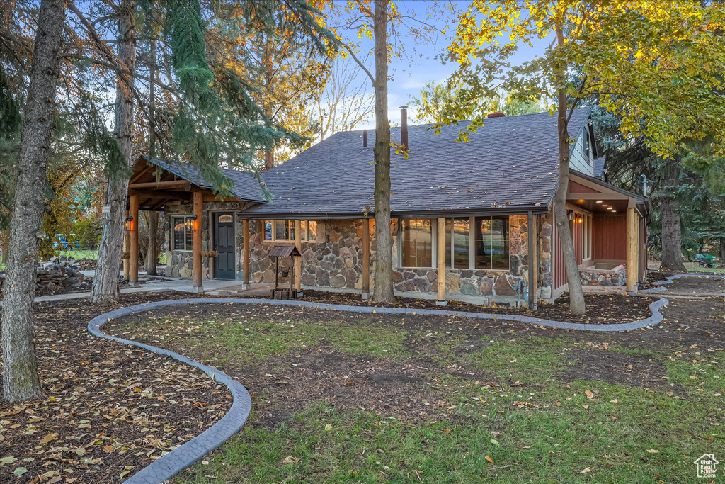 Rear view of property with a shingled roof, a patio area, stone siding, and a lawn