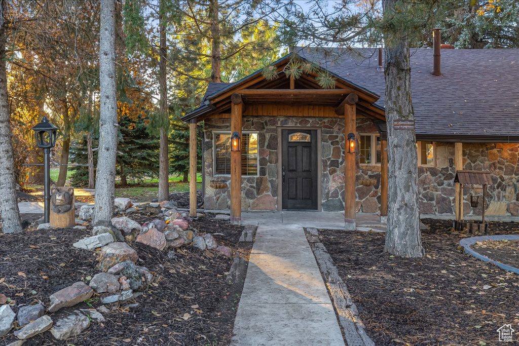 View of exterior entry featuring stone siding and a shingled roof