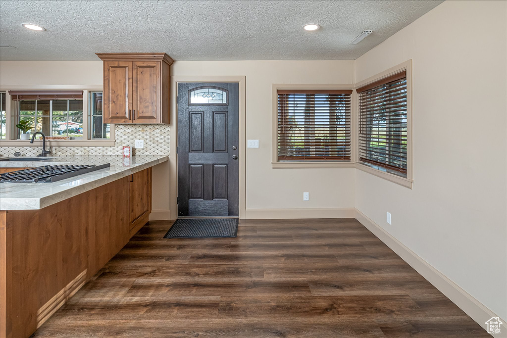 Kitchen featuring brown cabinets, dark wood-type flooring, a textured ceiling, decorative backsplash, and recessed lighting
