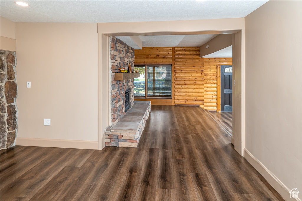 Unfurnished living room featuring log walls, wood finished floors, a fireplace, and a textured ceiling