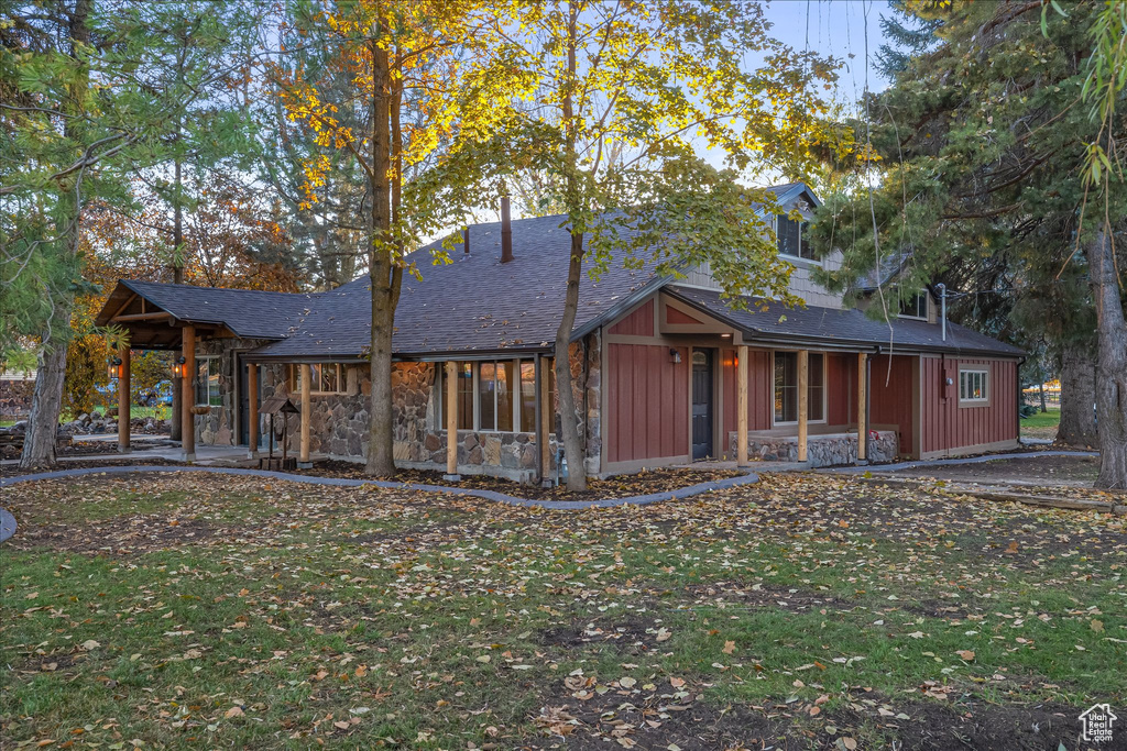 Back of house with a lawn, stone siding, board and batten siding, and a shingled roof