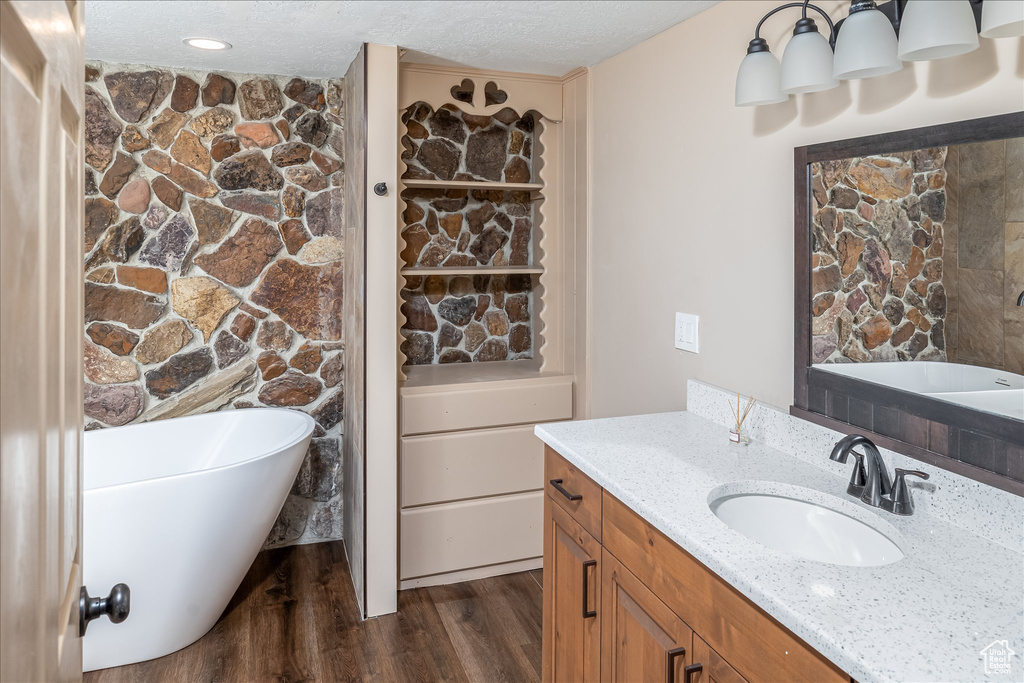 Full bathroom with a soaking tub, vanity, wood finished floors, and a textured ceiling