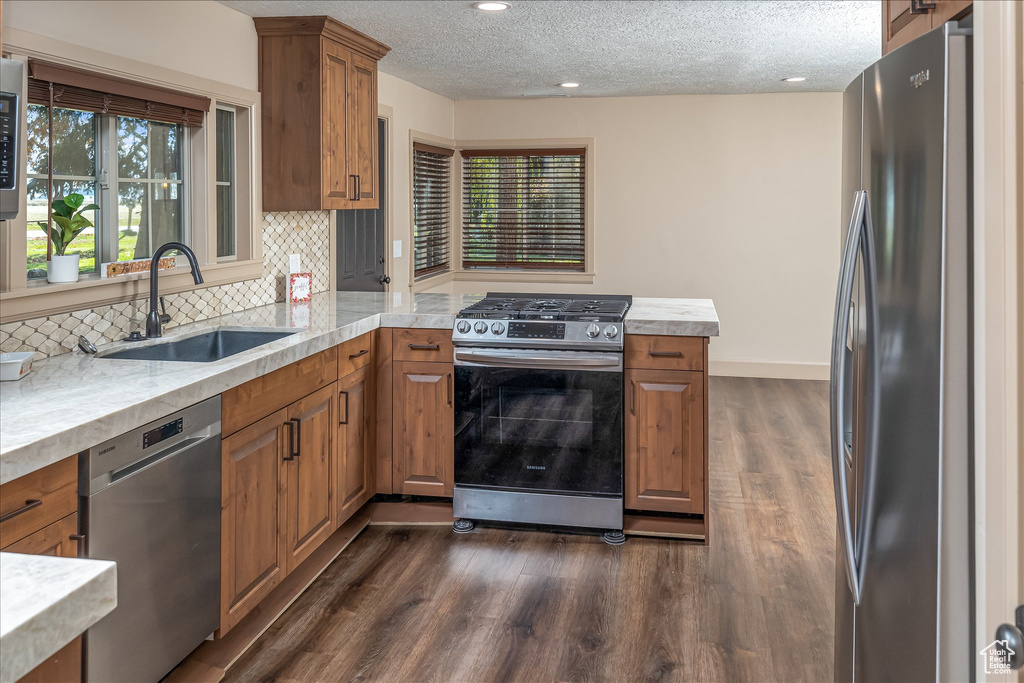 Kitchen with stainless steel appliances, brown cabinetry, a peninsula, light countertops, and a textured ceiling