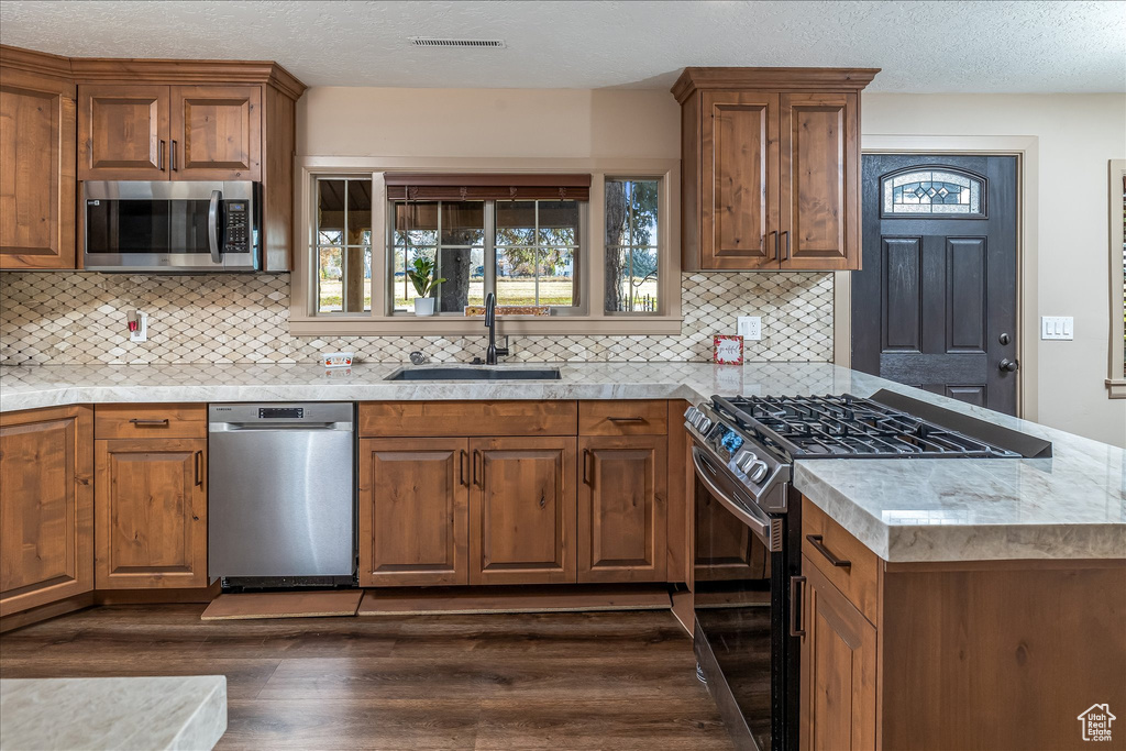 Kitchen featuring stainless steel appliances, dark wood-type flooring, brown cabinetry, decorative backsplash, and a peninsula