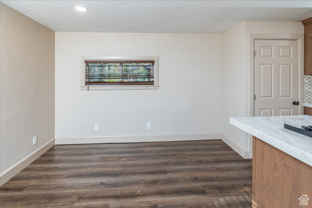 Empty room with a textured ceiling, dark wood-style floors, and recessed lighting