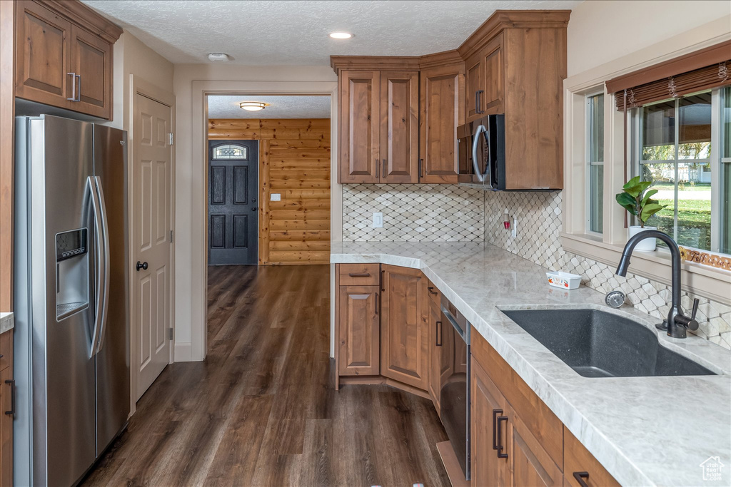 Kitchen featuring appliances with stainless steel finishes, dark wood finished floors, brown cabinetry, a textured ceiling, and backsplash