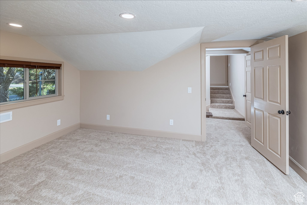 Additional living space with a textured ceiling, carpet, lofted ceiling, stairway, and recessed lighting