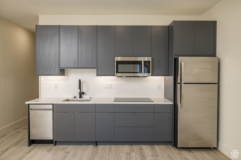 Kitchen featuring stainless steel appliances, baseboards, a sink, gray cabinets, and light countertops
