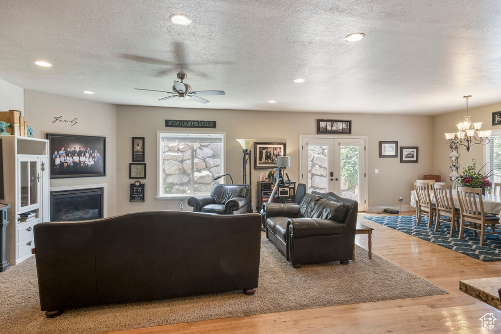 Living room featuring a chandelier, wood finished floors, a ceiling fan, a textured ceiling, and french doors