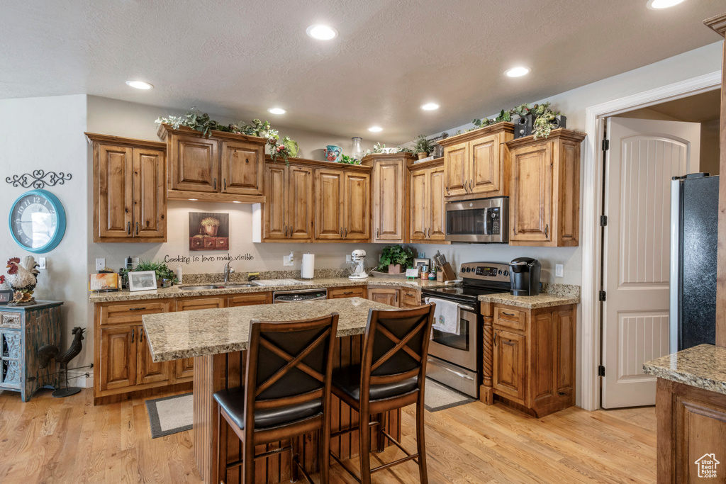 Kitchen with appliances with stainless steel finishes, light wood-style floors, brown cabinets, and recessed lighting