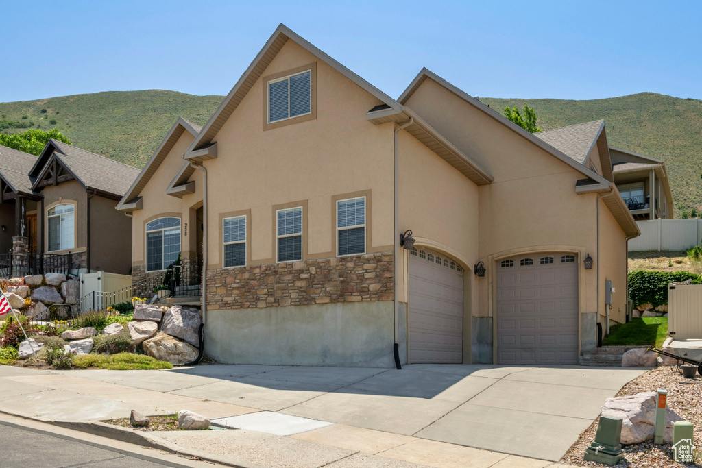 View of front of home featuring stone siding, a mountain view, concrete driveway, a garage, and stucco siding