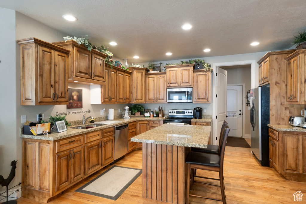 Kitchen with stainless steel appliances, a kitchen island, recessed lighting, light wood-style floors, and brown cabinets