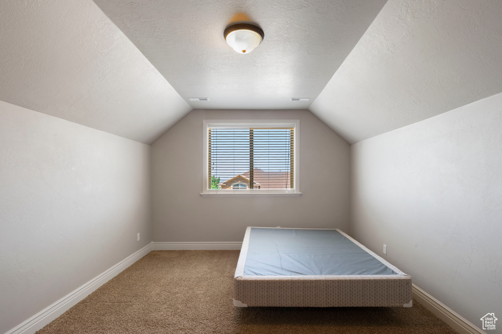 Unfurnished bedroom featuring carpet floors, lofted ceiling, and a textured ceiling
