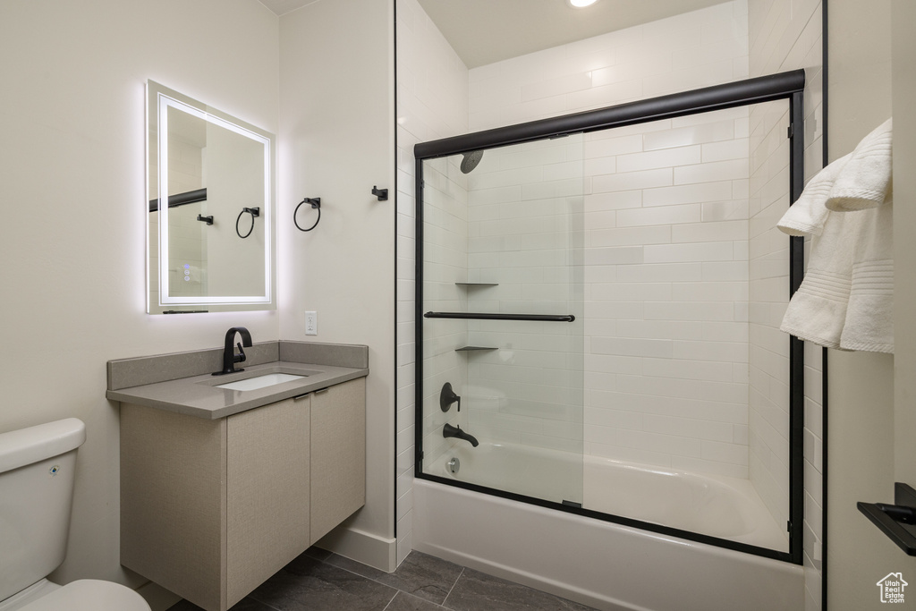 Bathroom featuring toilet, bath / shower combo with glass door, and vanity
