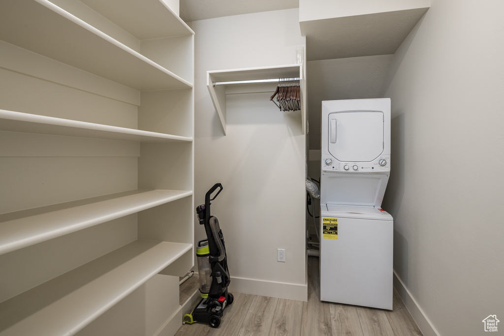 Washroom with stacked washer and clothes dryer, wood finished floors, and baseboards
