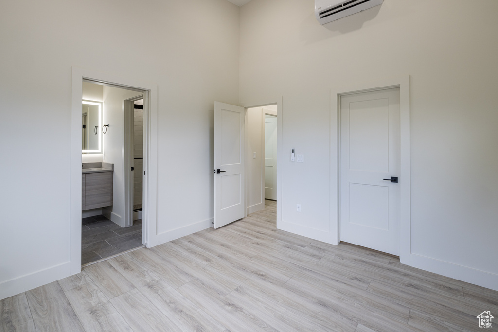 Unfurnished bedroom featuring a towering ceiling, light wood-type flooring, a wall mounted AC, baseboards, and ensuite bath
