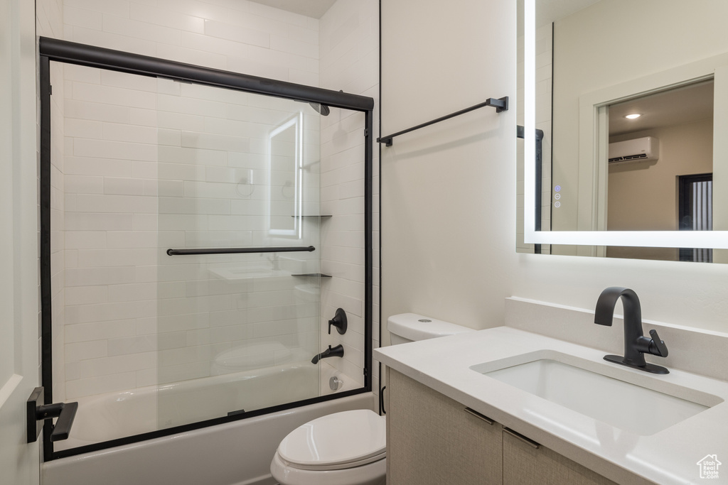 Full bathroom with toilet, an AC wall unit, vanity, and bath / shower combo with glass door