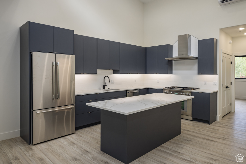 Kitchen with stainless steel appliances, wall chimney range hood, a sink, light wood finished floors, and backsplash