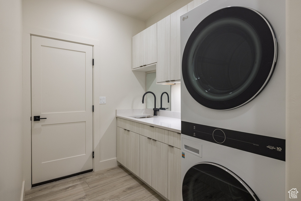 Laundry area with estacked washer and dryer, cabinet space, light wood finished floors, and baseboards