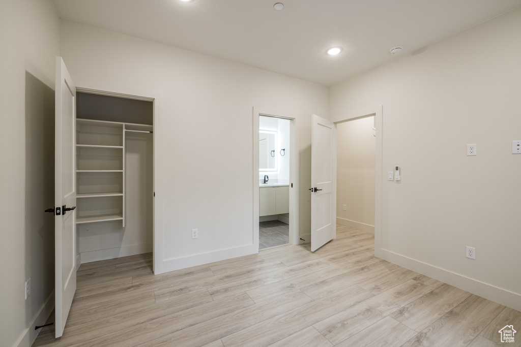 Unfurnished bedroom featuring a walk in closet, baseboards, light wood-style flooring, a closet, and recessed lighting