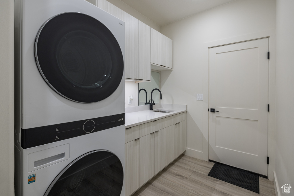 Laundry area with stacked washing machine and dryer, cabinet space, light wood-style flooring, and baseboards