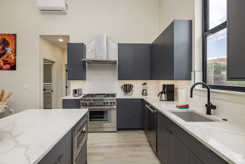 Kitchen with wall chimney range hood, a sink, stainless steel appliances, backsplash, and a high ceiling