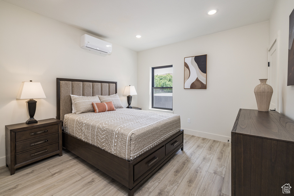 Bedroom with a wall mounted air conditioner, light wood-type flooring, baseboards, and recessed lighting