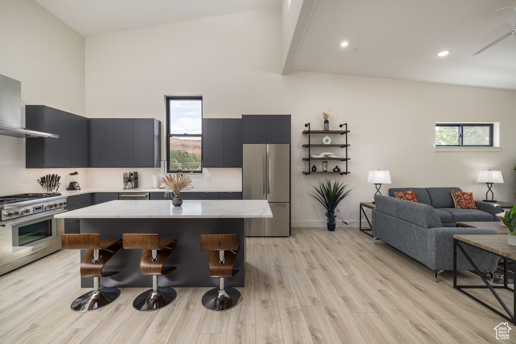 Kitchen with appliances with stainless steel finishes, high vaulted ceiling, a breakfast bar area, light wood-style flooring, and a center island