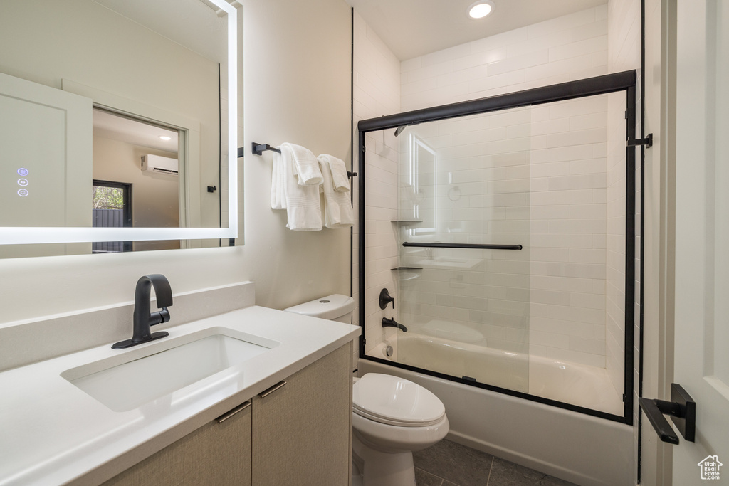 Bathroom featuring a wall mounted air conditioner, toilet, vanity, bath / shower combo with glass door, and tile patterned flooring