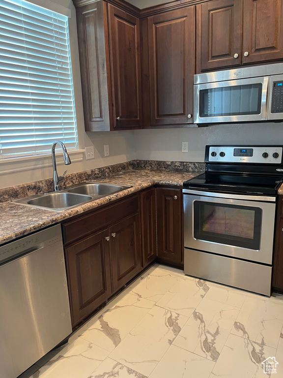 Kitchen with stainless steel appliances, light marble finish floors, dark countertops, and dark brown cabinetry