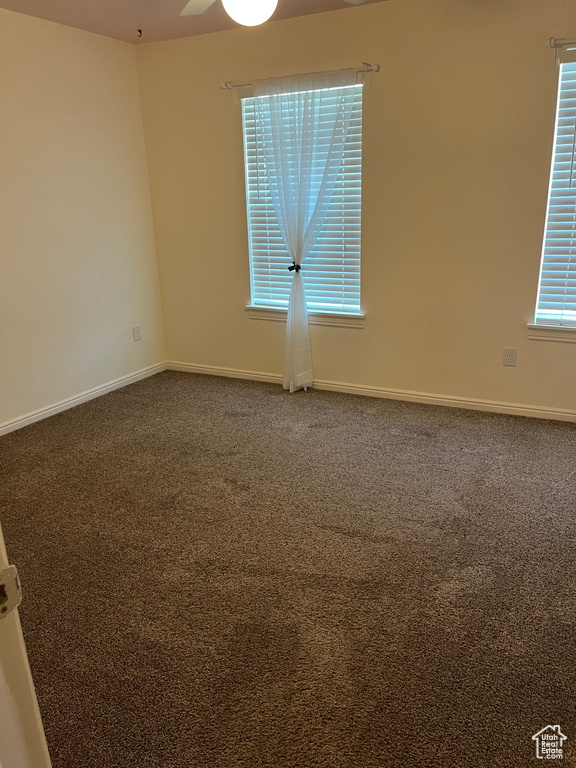 Empty room featuring dark carpet and a ceiling fan