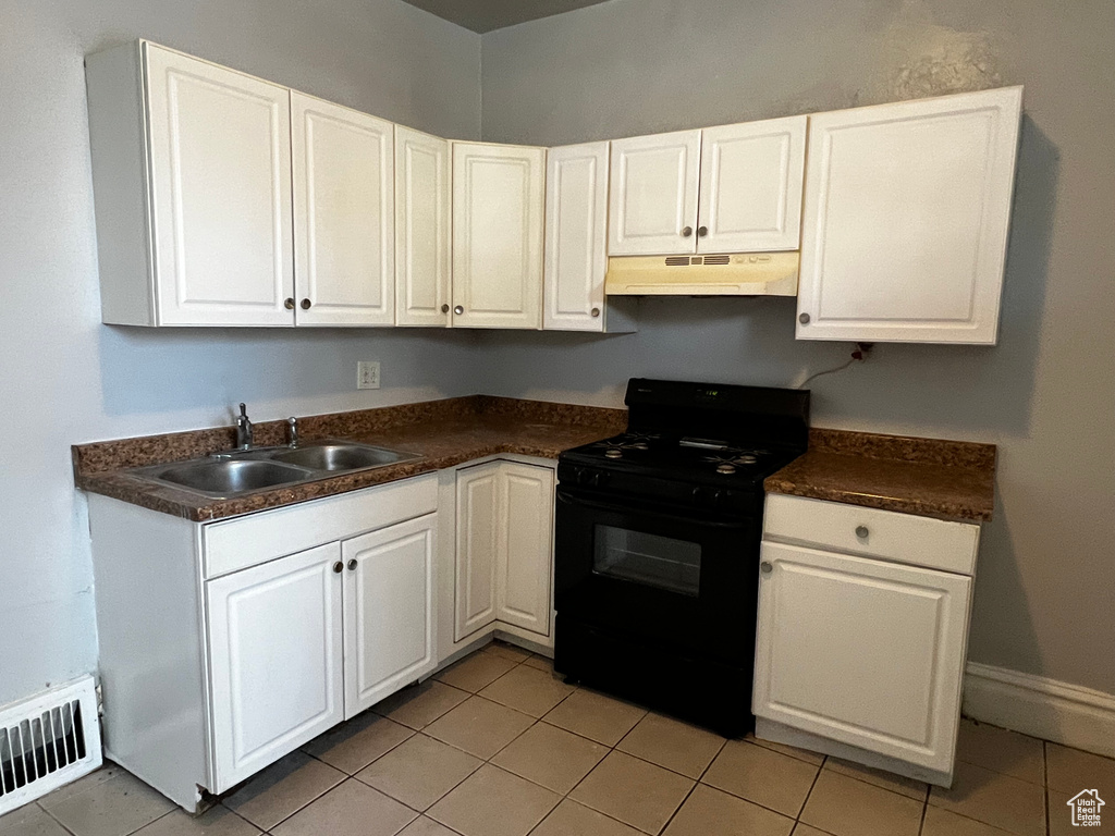 Kitchen with black range, under cabinet range hood, dark countertops, white cabinets, and light tile patterned floors