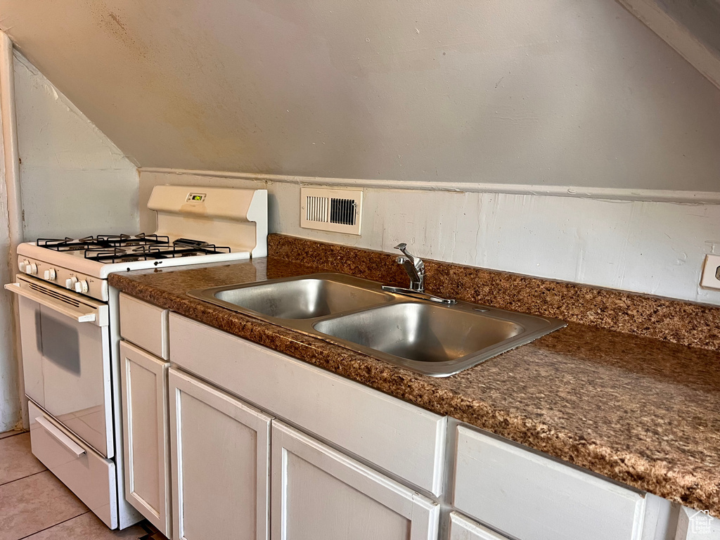 Kitchen featuring white range with gas cooktop, dark countertops, white cabinetry, light tile patterned floors, and lofted ceiling