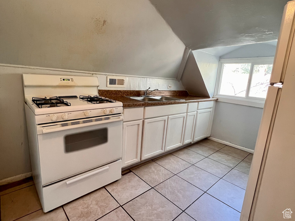 Kitchen with white appliances, vaulted ceiling, light tile patterned floors, dark countertops, and white cabinetry