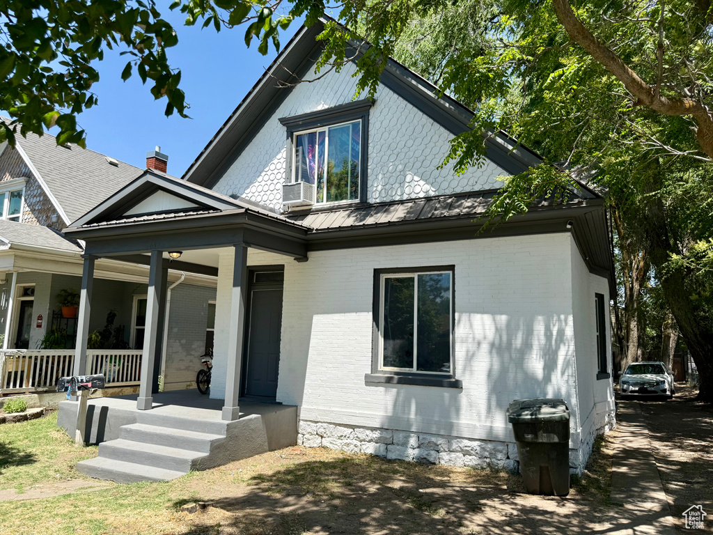 View of front facade featuring a porch, brick siding, and a metal roof