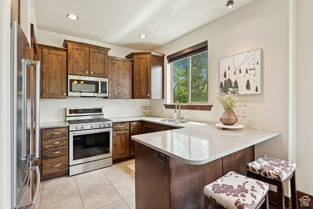 Kitchen featuring stainless steel appliances, a peninsula, light countertops, a breakfast bar area, and light tile patterned floors