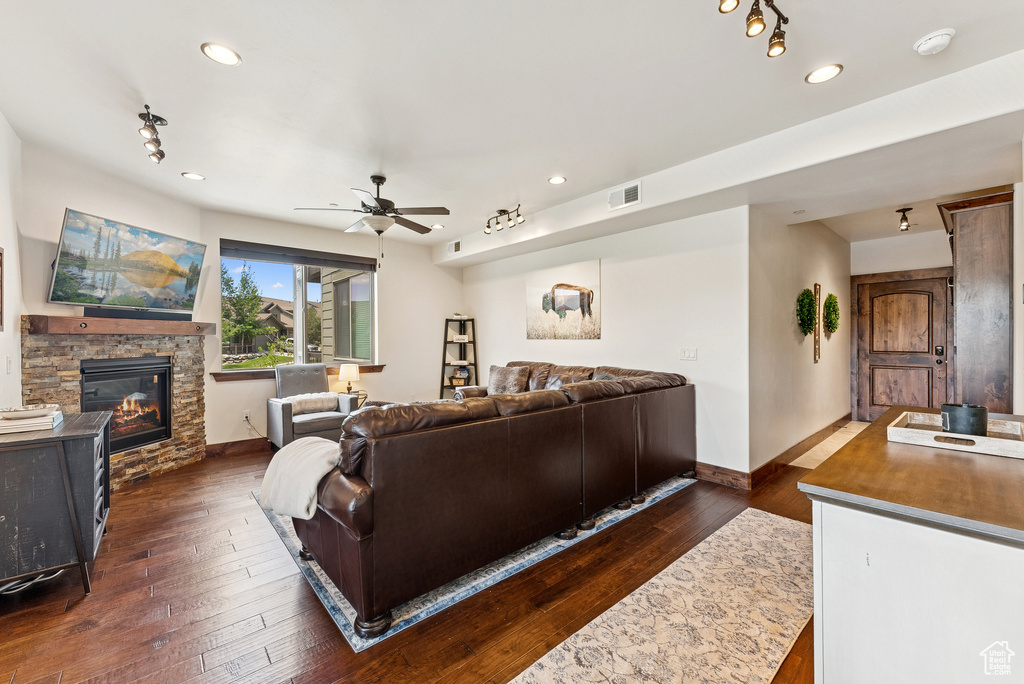 Living room with a stone fireplace, ceiling fan, dark wood-style floors, and recessed lighting