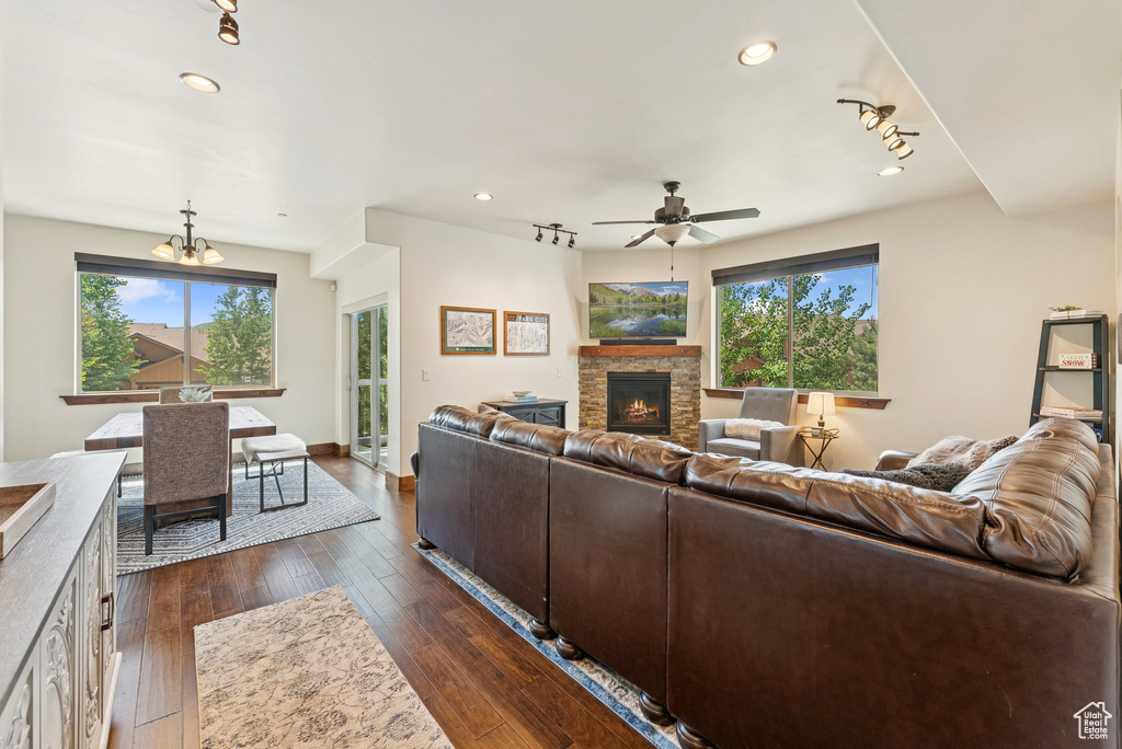 Living room with a stone fireplace, a ceiling fan, recessed lighting, dark wood-type flooring, and a chandelier