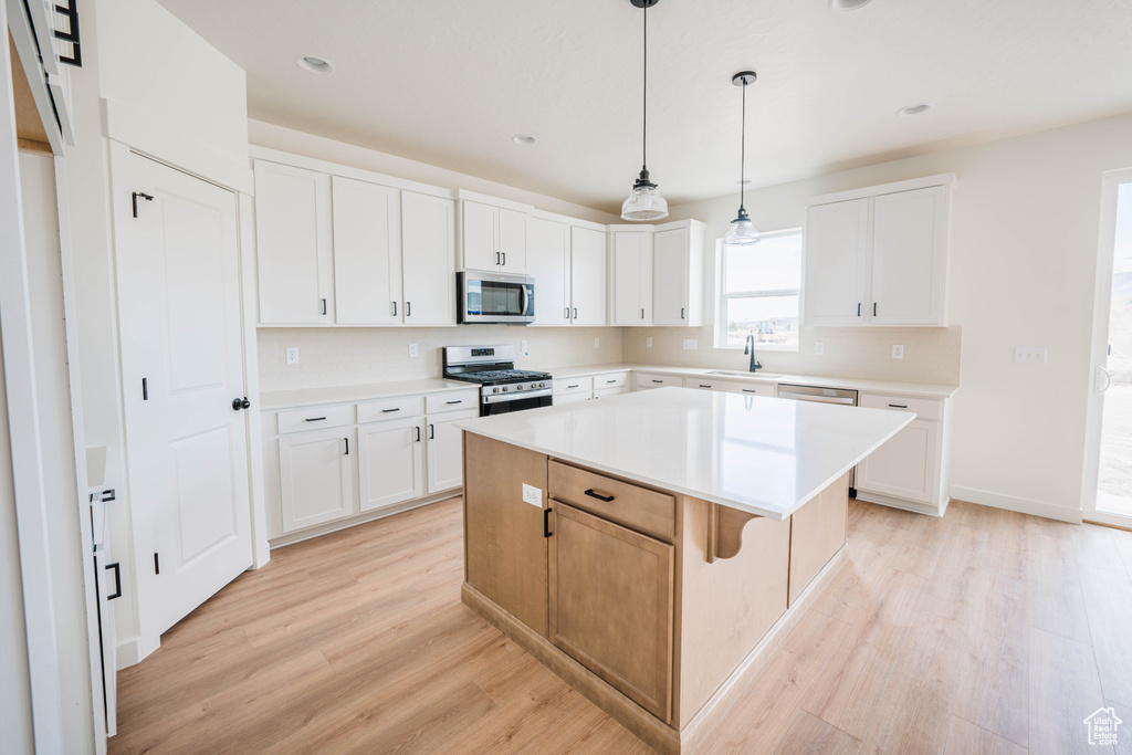 Kitchen featuring stainless steel appliances, light wood-style flooring, a center island, light countertops, and white cabinets