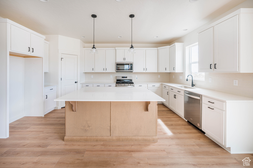 Kitchen featuring appliances with stainless steel finishes, a kitchen island, light wood finished floors, a breakfast bar area, and recessed lighting