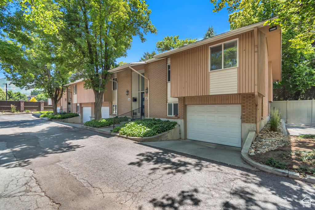 Raised ranch featuring an attached garage, asphalt driveway, and brick siding