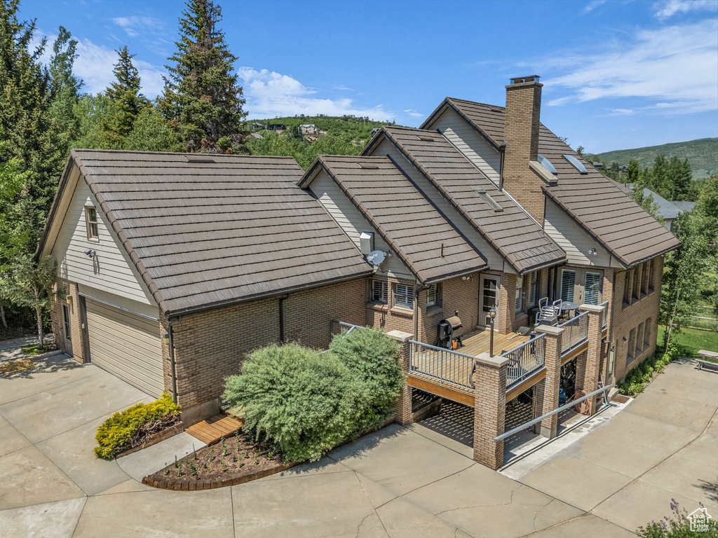 Rear view of property featuring brick siding, concrete driveway, a wooden deck, and a chimney