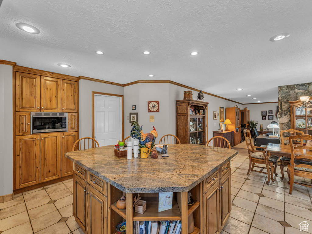 Kitchen with open shelves, stainless steel microwave, ornamental molding, light tile patterned flooring, and brown cabinetry