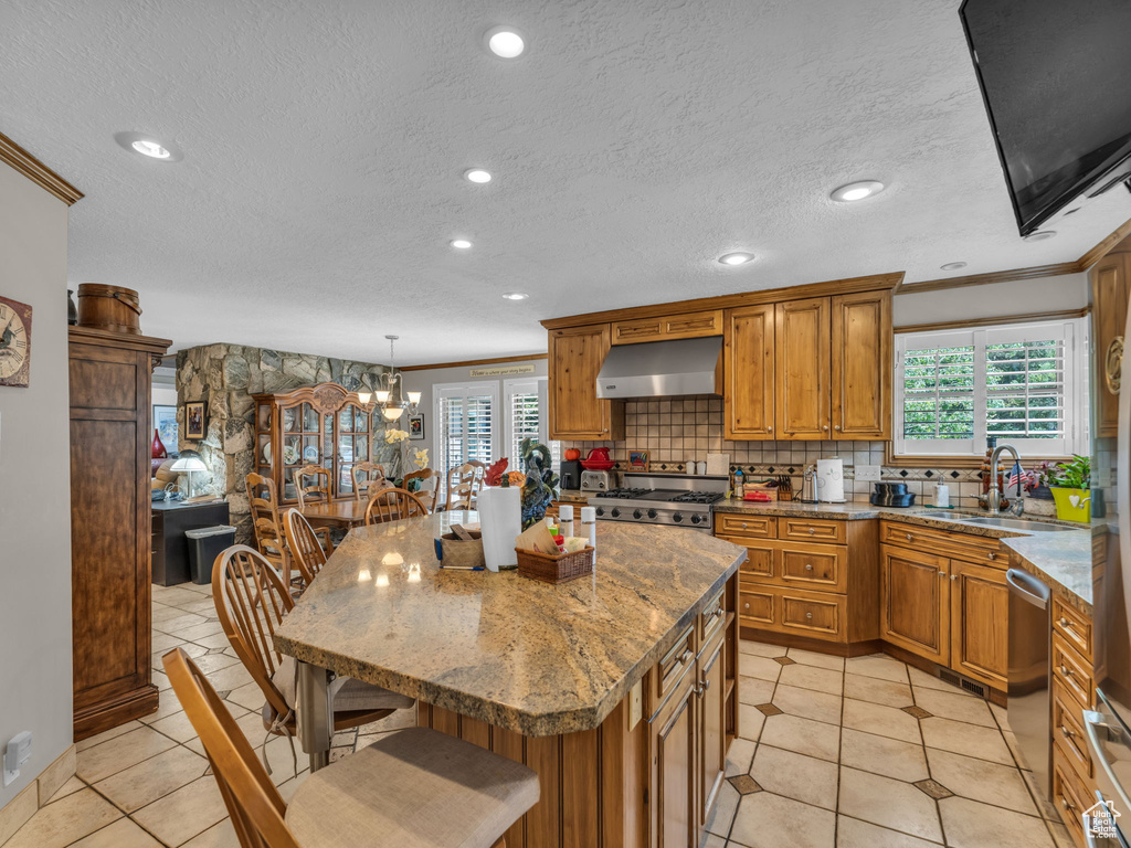 Kitchen with extractor fan, brown cabinets, stainless steel dishwasher, a breakfast bar area, and crown molding